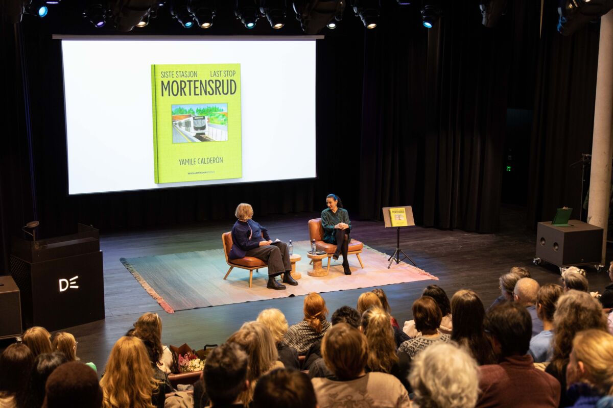 Samtale mellom to personer på en scene i et bibliotek. Foto.