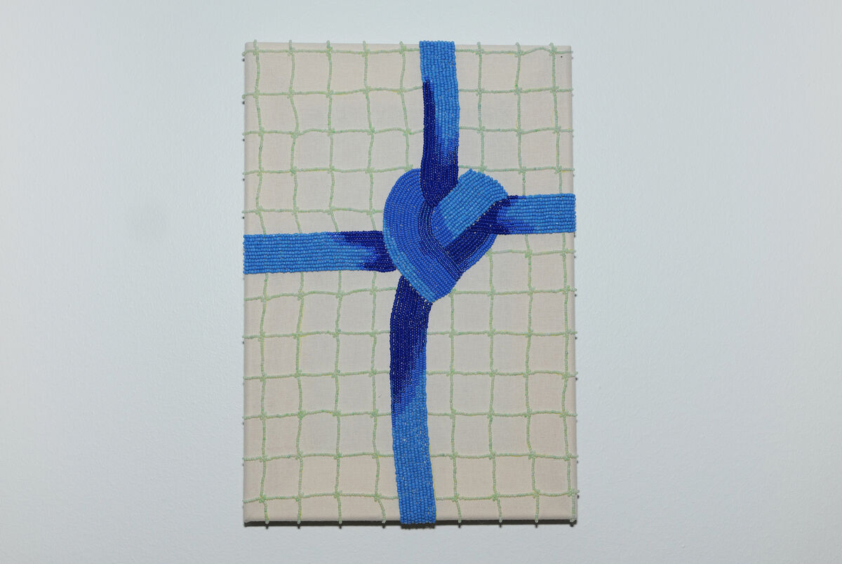 Et firkantet lerret med en perlet, grønn bakgrunn. I front er en perlet, blå knute. Foto.
