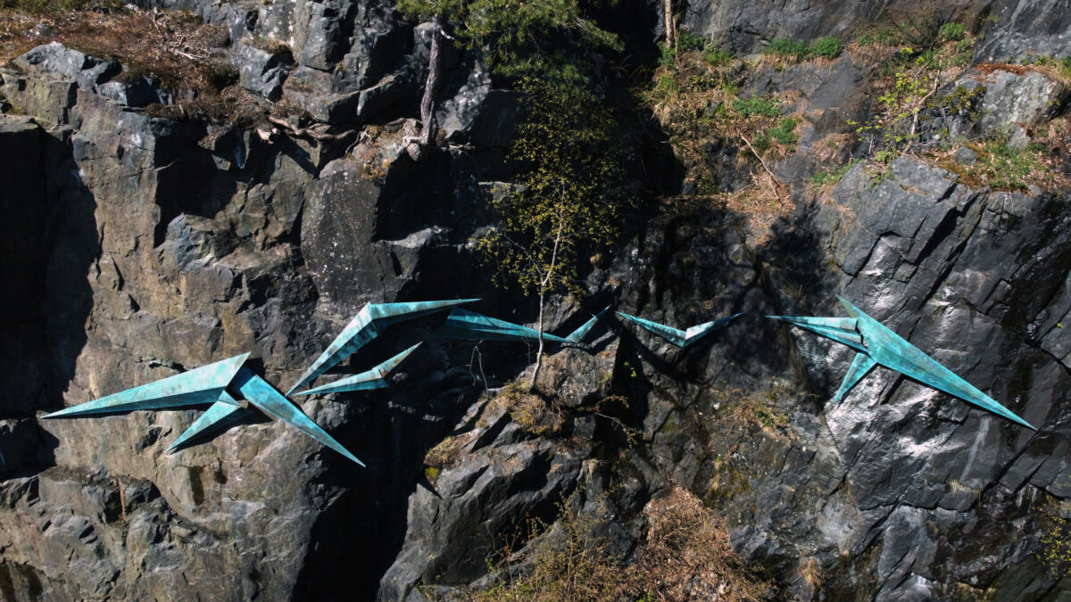 Geometriske fuglelignende skulpturfigurer som ser ut til å fly over berg. Foto.