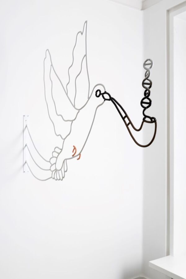 En stålskulptur av en due som røyker pipe. Skulpturen henger ut fra veggen. Foto av skulptur som henger på vegg.