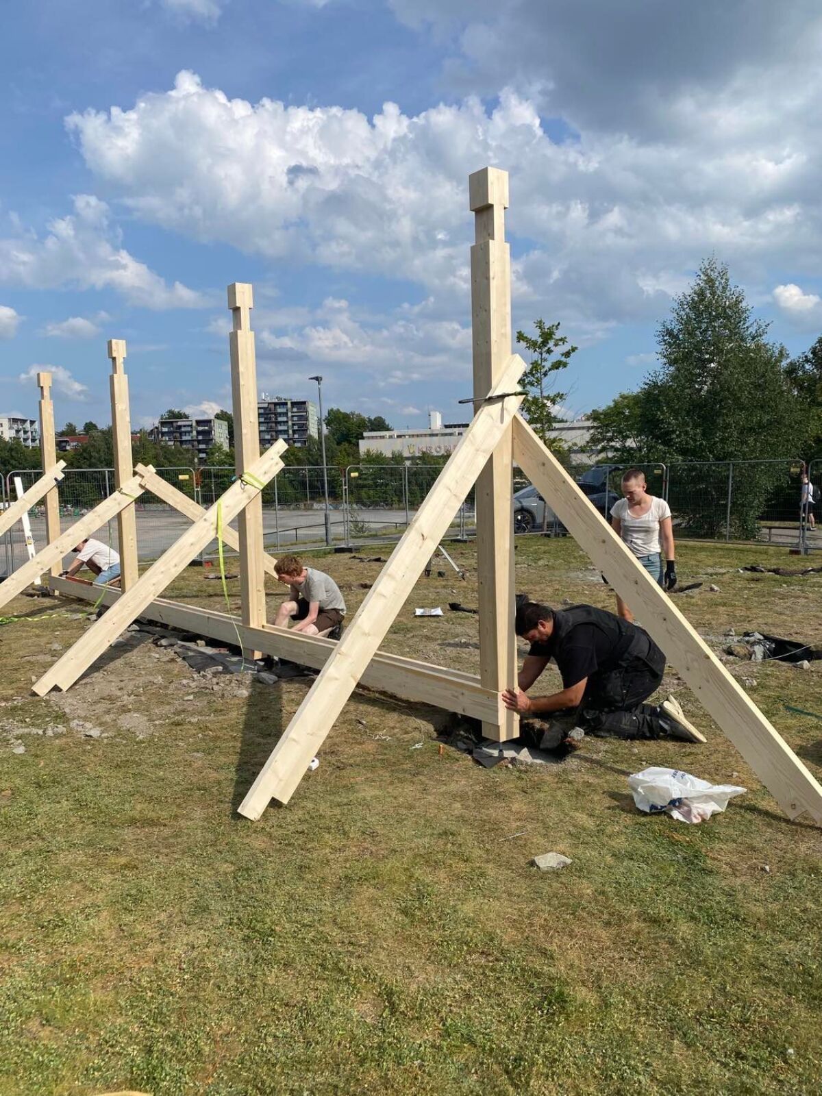 Fire personer er utendørs på en gressplen og bygger en trekonstruksjon. Foto.