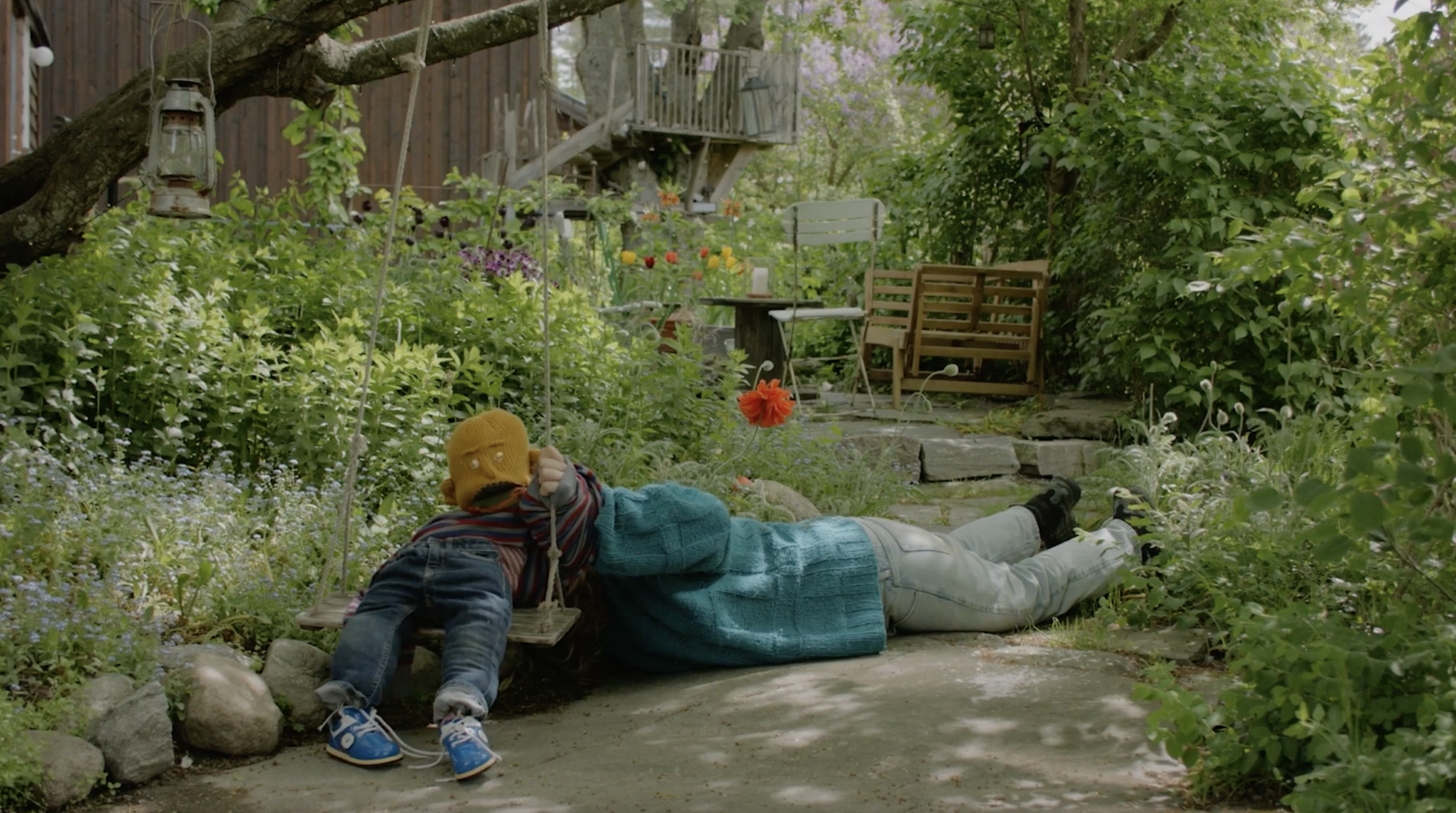 Barn og voksen ligger på bakken i en hage. Foto.