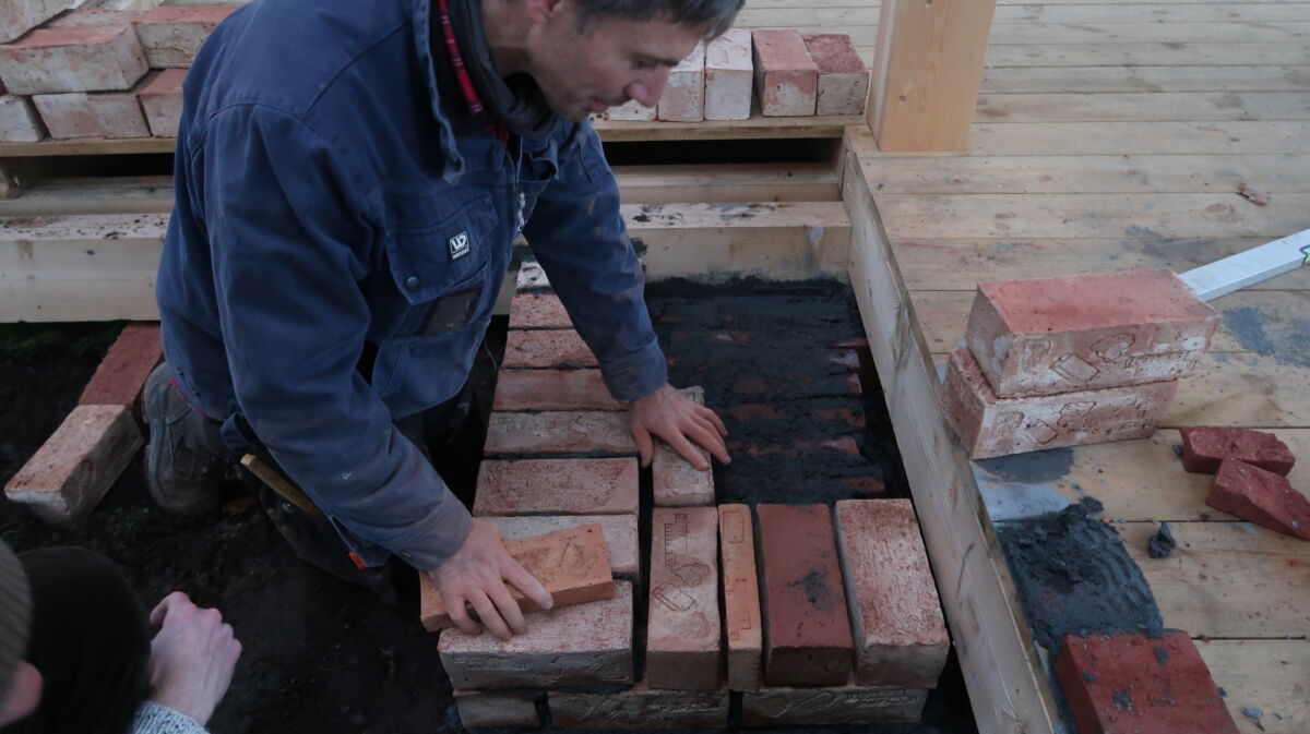 En person jobber med å legge murstein. Foto.