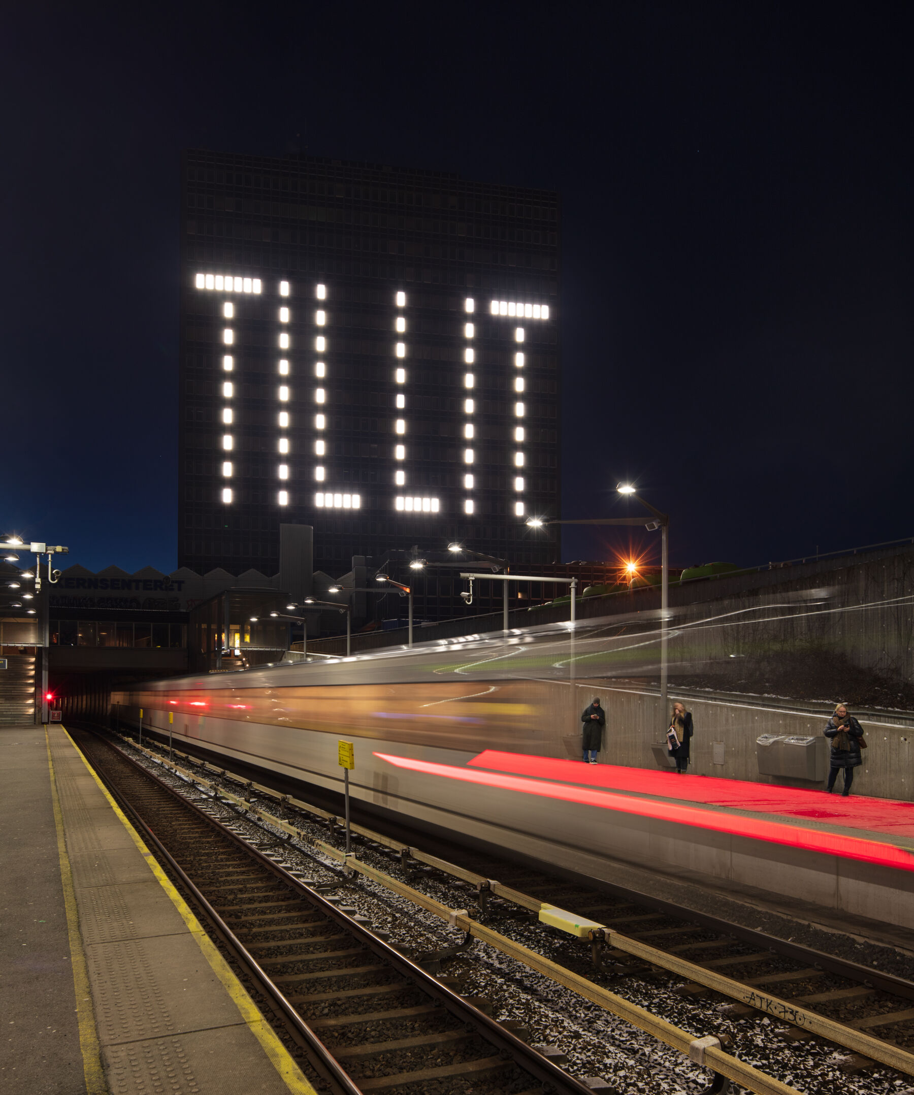 Høyblokk med mange vinduer. Noen av vinduene lyses opp, slik at ordet "TILLIT" står skrevet på bygningen. Foto.