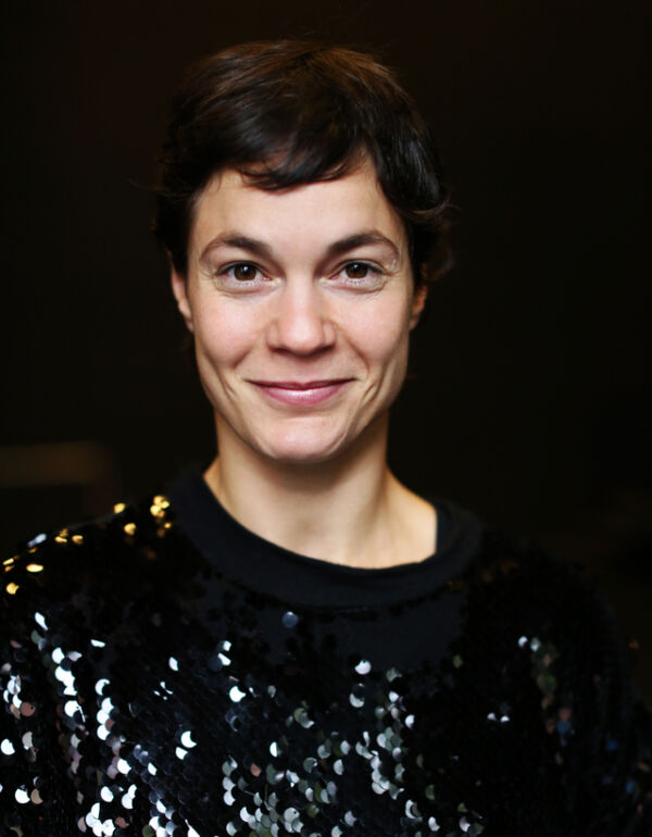 Portrettfoto av en person med glitrende genser og mørkt, kort hår som ser rett i kamera og smiler mildt. Foto.