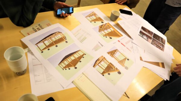 Flere tegninger av en paviljong ligger utover et bord. Foto.