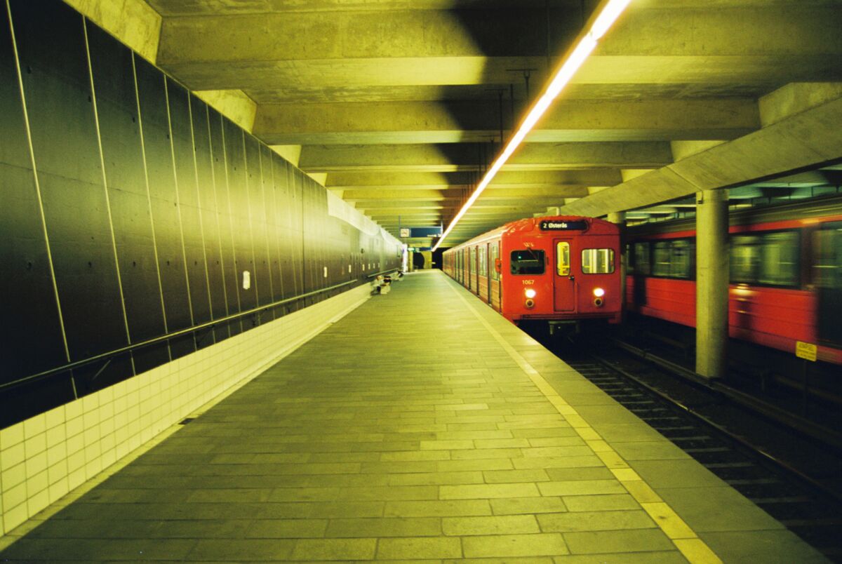 Interiør av t-banestasjon. En rød T-banevogn kjører inn på perrongen. En annen kjører ut. Foto.
