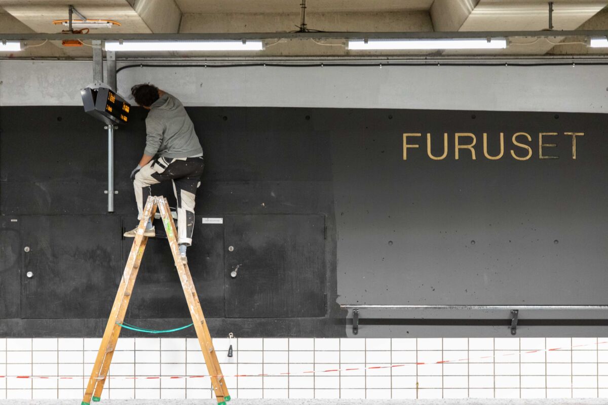 Person maler opp veggen innendørs på en T-baneplattform. Foto.