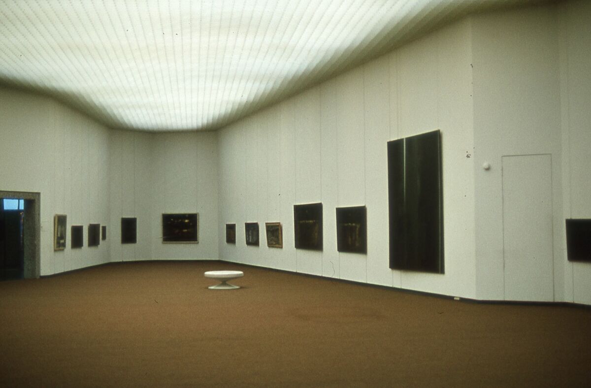 Utstillingsrom med store, mørke malerier hengende på hvit vegg. Foto.