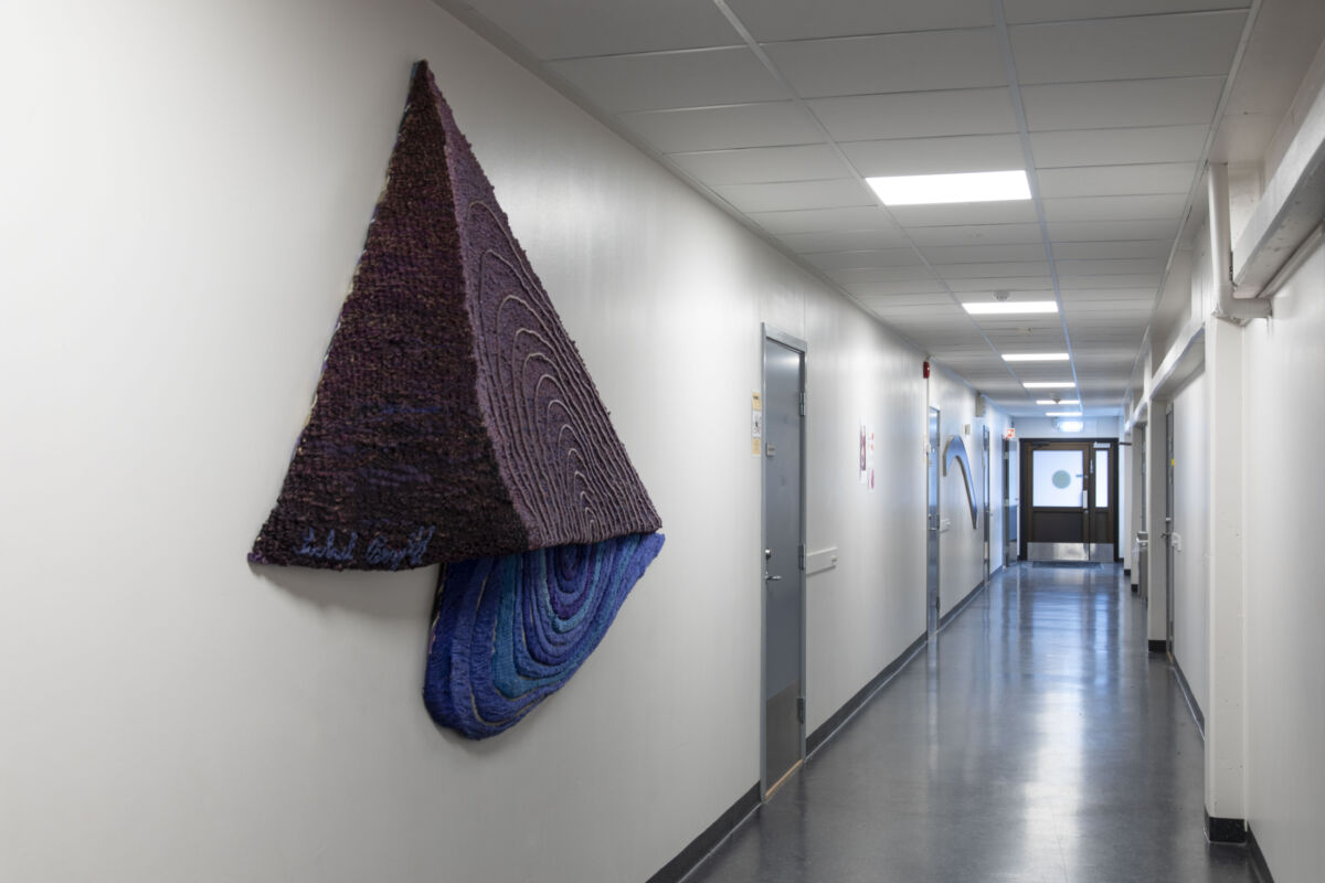 Tekstilverk hengende på en korridorvegg. Foto.