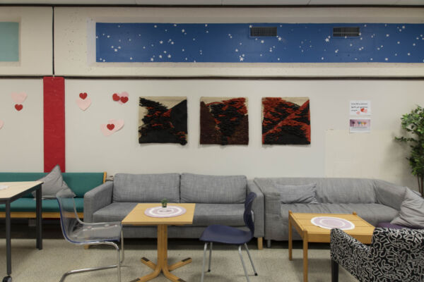 Tre tekstilverk på vegg med sofagruppe i forgrunnen. Foto.