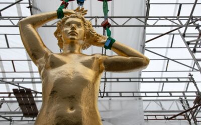 Utsnitt av en stor, gullforgylt skulptur av en kvinne sett forfra. Skulpturen står inne i et telt med stillaser rundt. Foto.