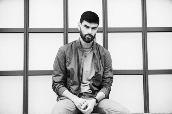 Portrett bilde i svart-hvitt av en person som siter foran noen vinduer. Foto.