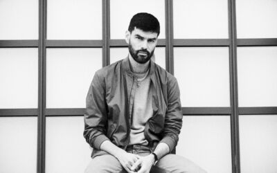 Portrett bilde i svart-hvitt av en person som siter foran noen vinduer. Foto.