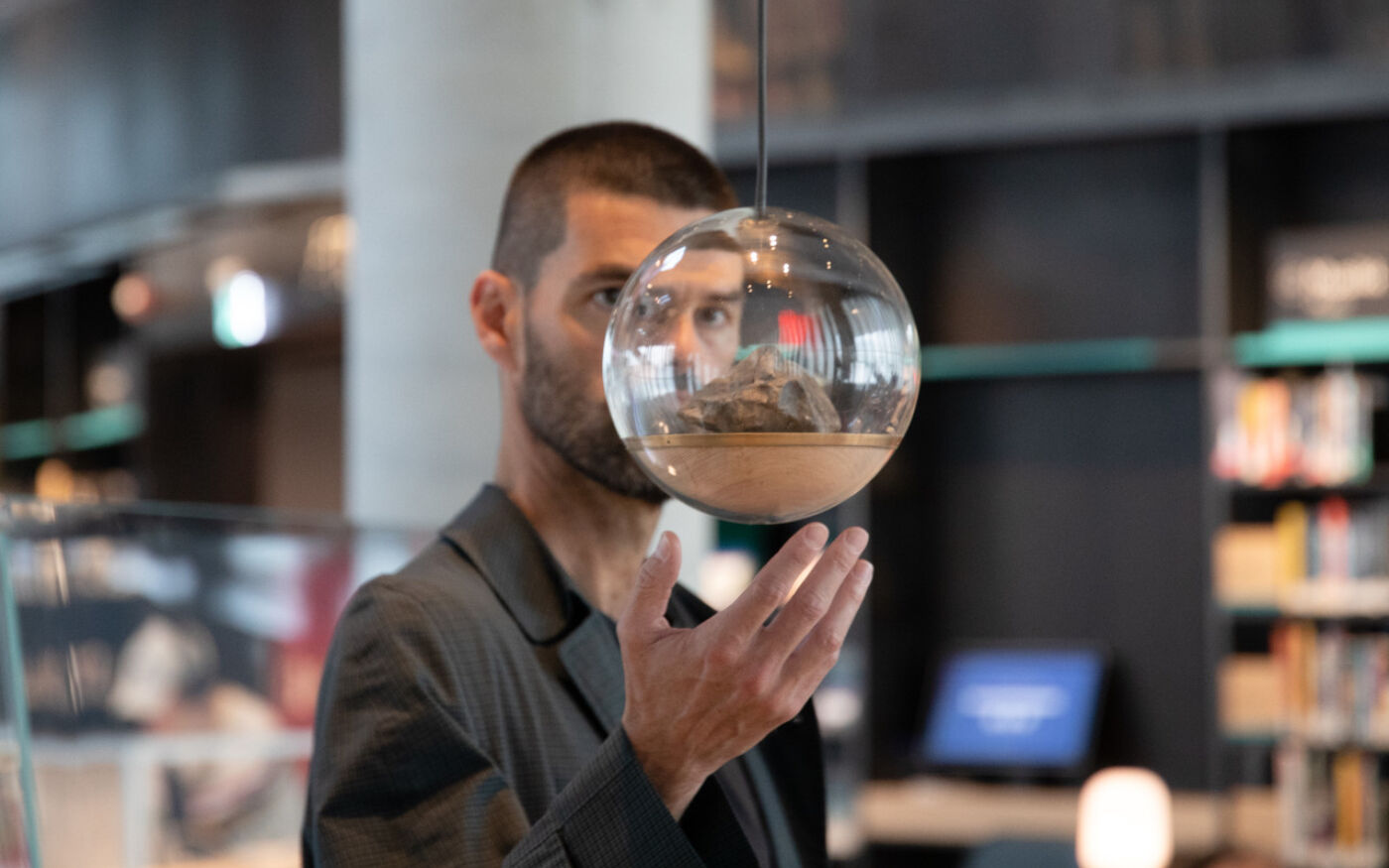 En person står bak en glasskule. Personen er inne på et bibliotek. Foto.