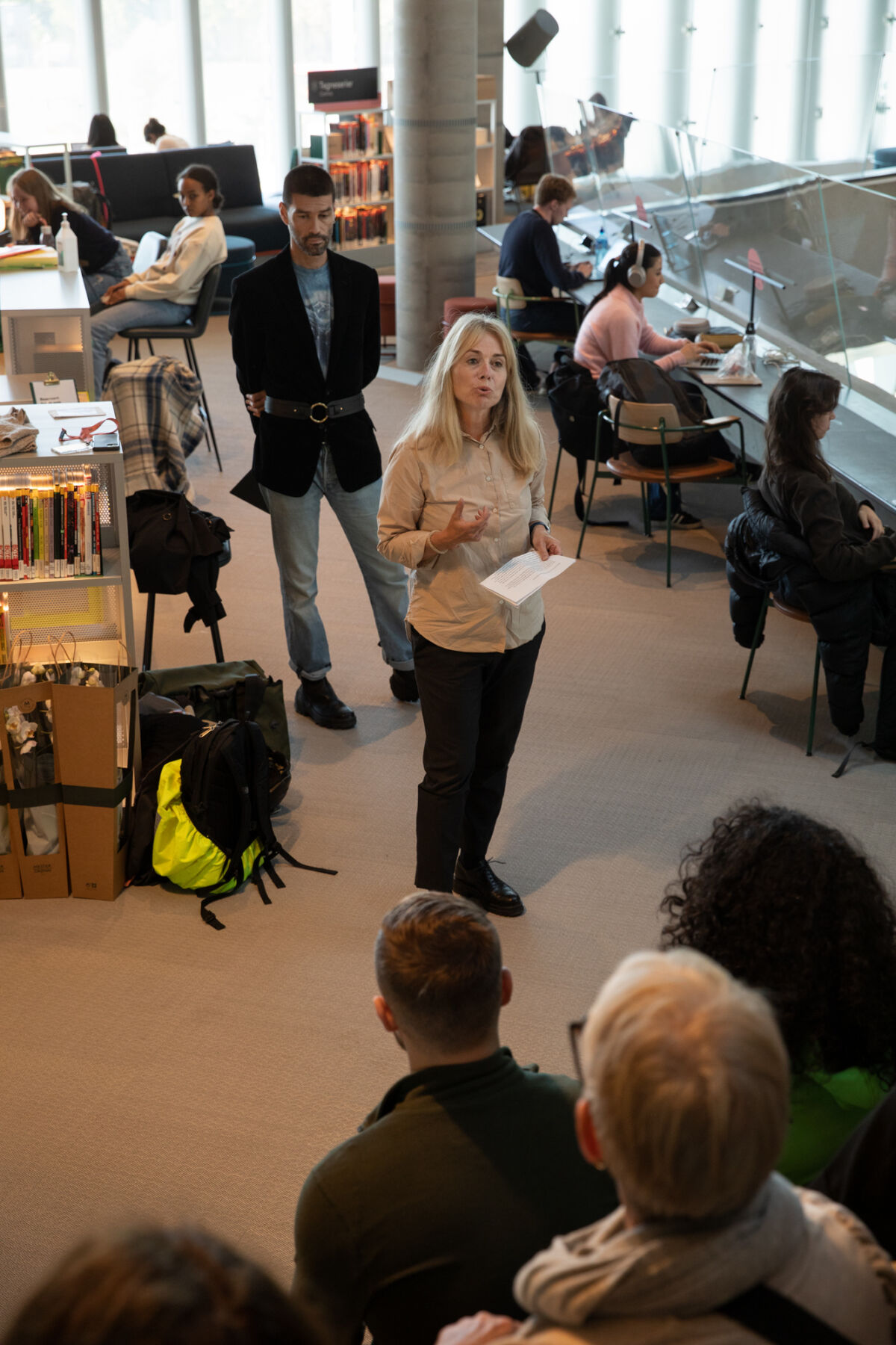 To personer står sammen foran en menneskemengde. De er inne i et bibliotek. Foto.