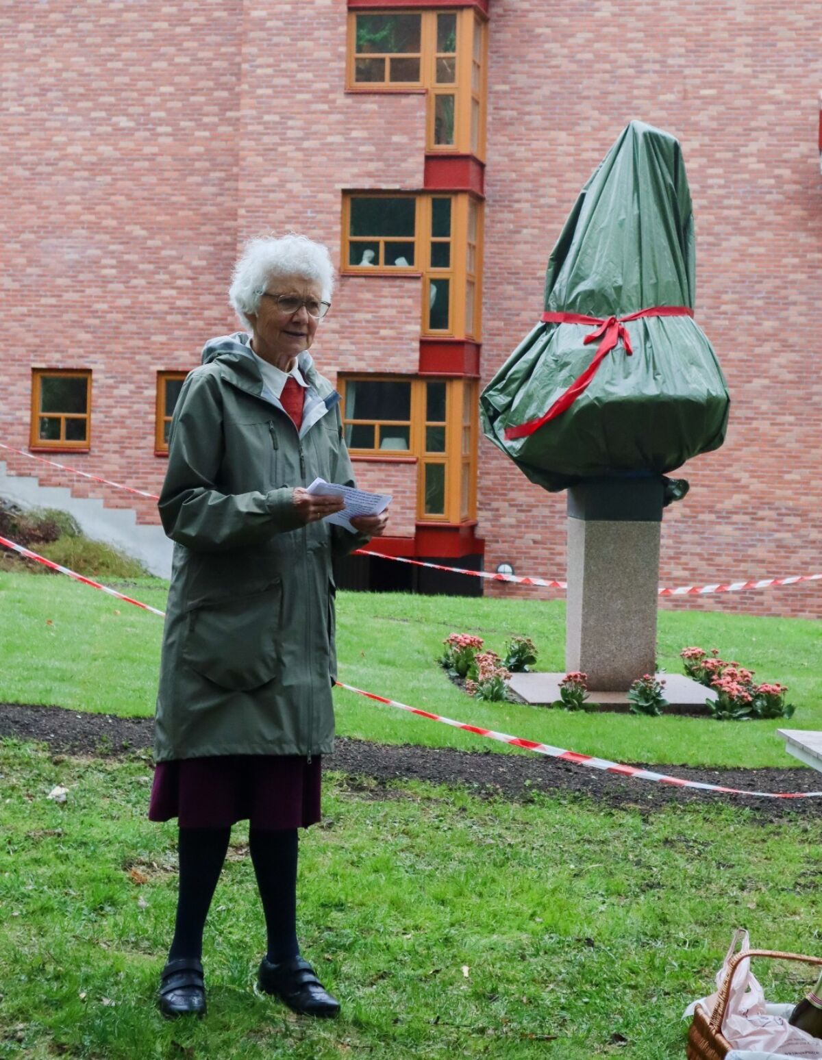 En person står foran en skulptur dekket til med en plastduk. Foto.