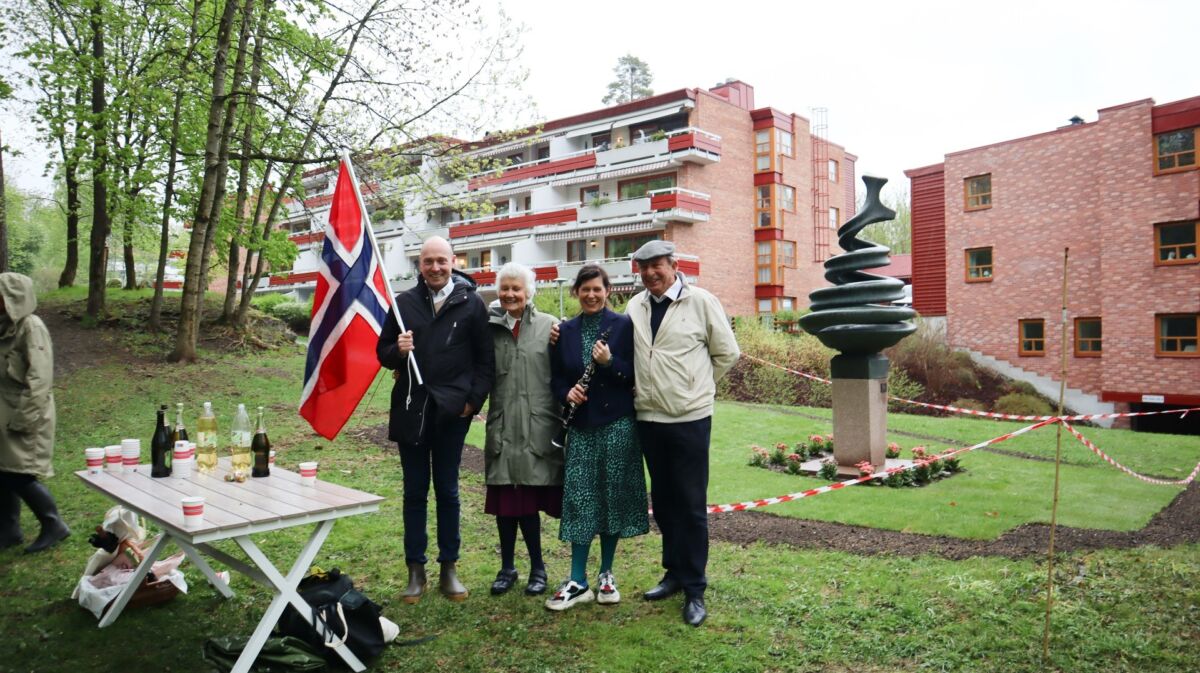 Fire personer står sammen utendørs. Den ene personen, ytterst til venstre, holder i et stort flagg. Foto.