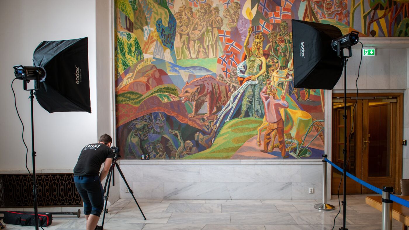 Person fotograferer muralmaleri i Oslo rådhus. Foto.