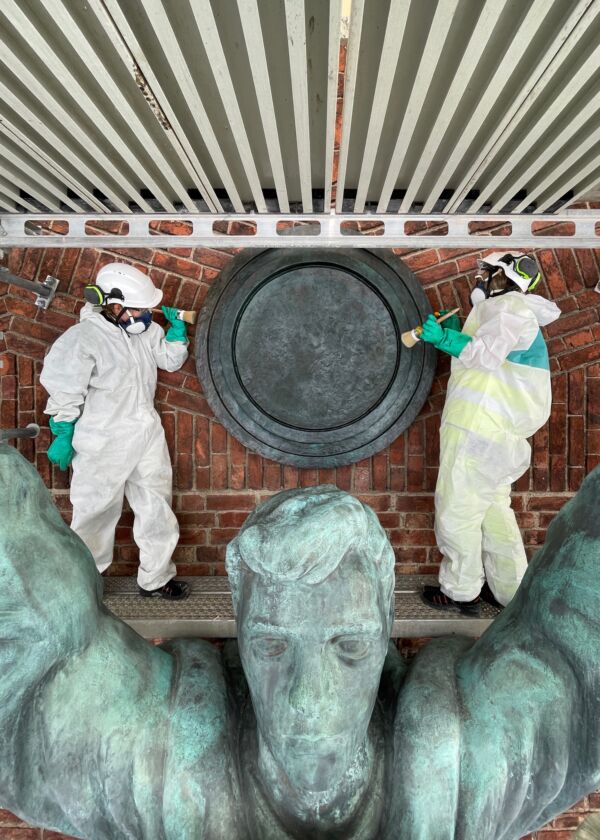 Foto av to personer som konserverer hodet på en skulptur.