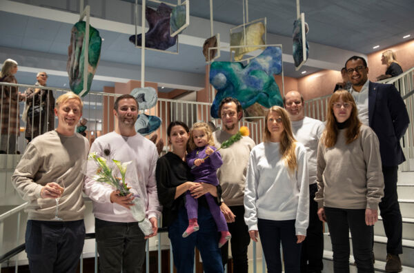 Mange personer står foran et kunstverk bestående av organiske former som henger fra taket. Foto.