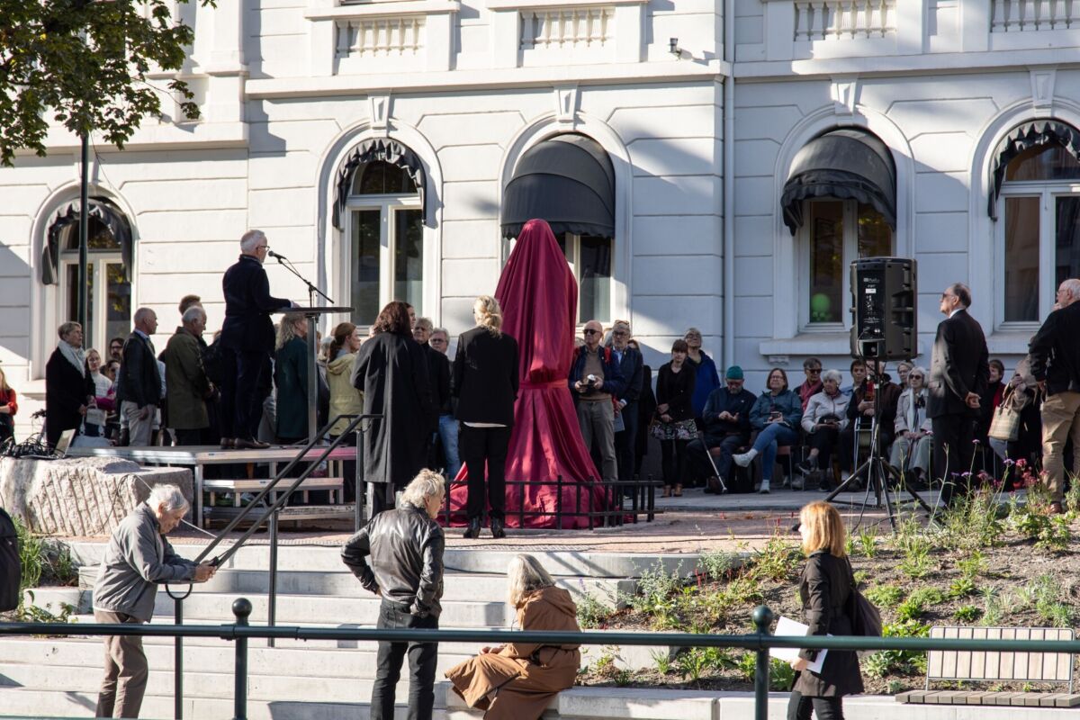 Flere mennesker står samlet sammen rundt en skulptur som er pakket inn i rød tekstil.