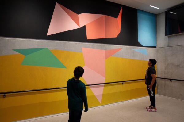To unge personer står og ser på et fargesterkt veggmaleri.