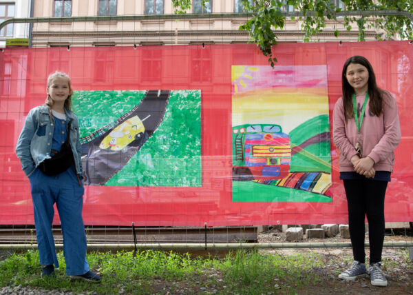 To barn står foran to store tegninger hengt opp på et gjerde. Foto.