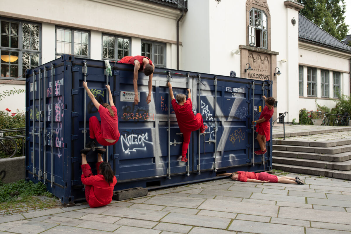 Seks personer kledd i rødt klatrer på en container. Foto.
