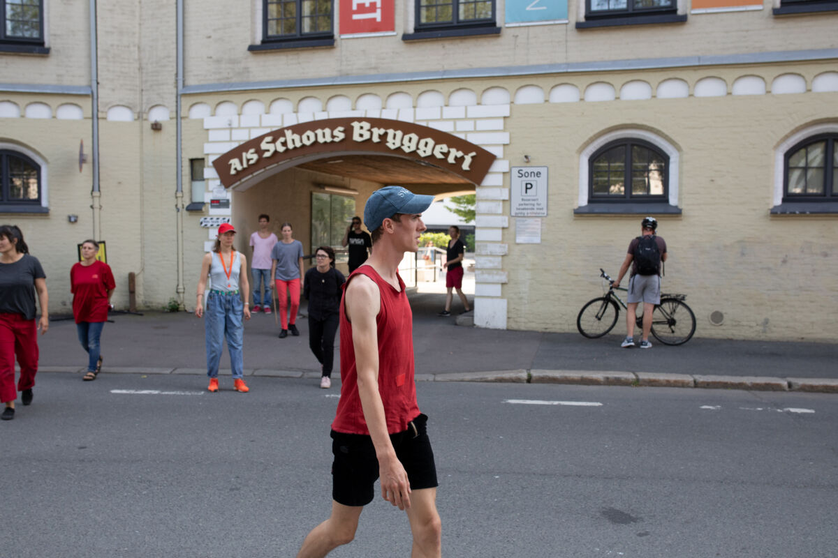 Person med rød singlet og caps går i en gate. Flere personer ser på. Foto.