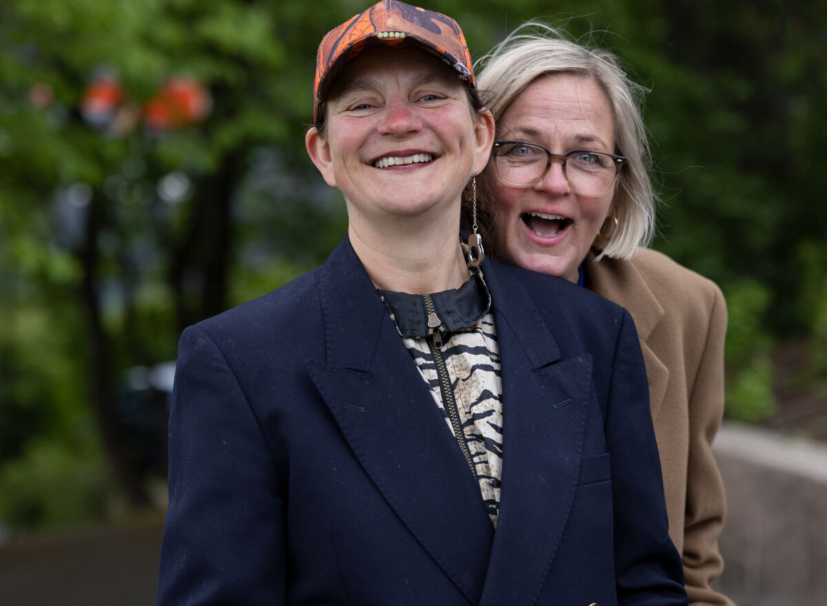 Portrettbilde av to personer som smiler mot kamera. De står foran grønne omgivelser. Foto.