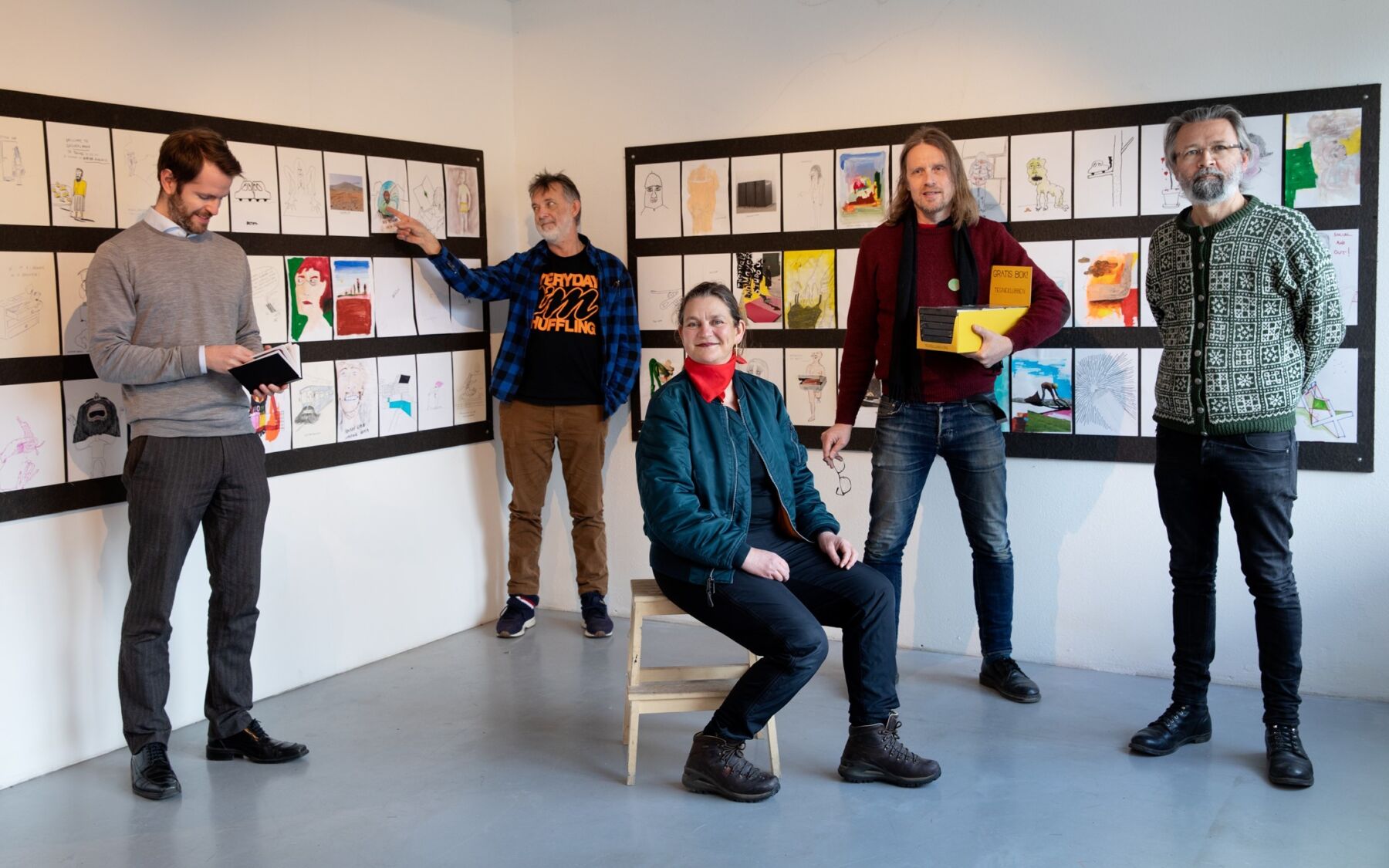 Fem personer fotografert foran mange tegninger. Foto.