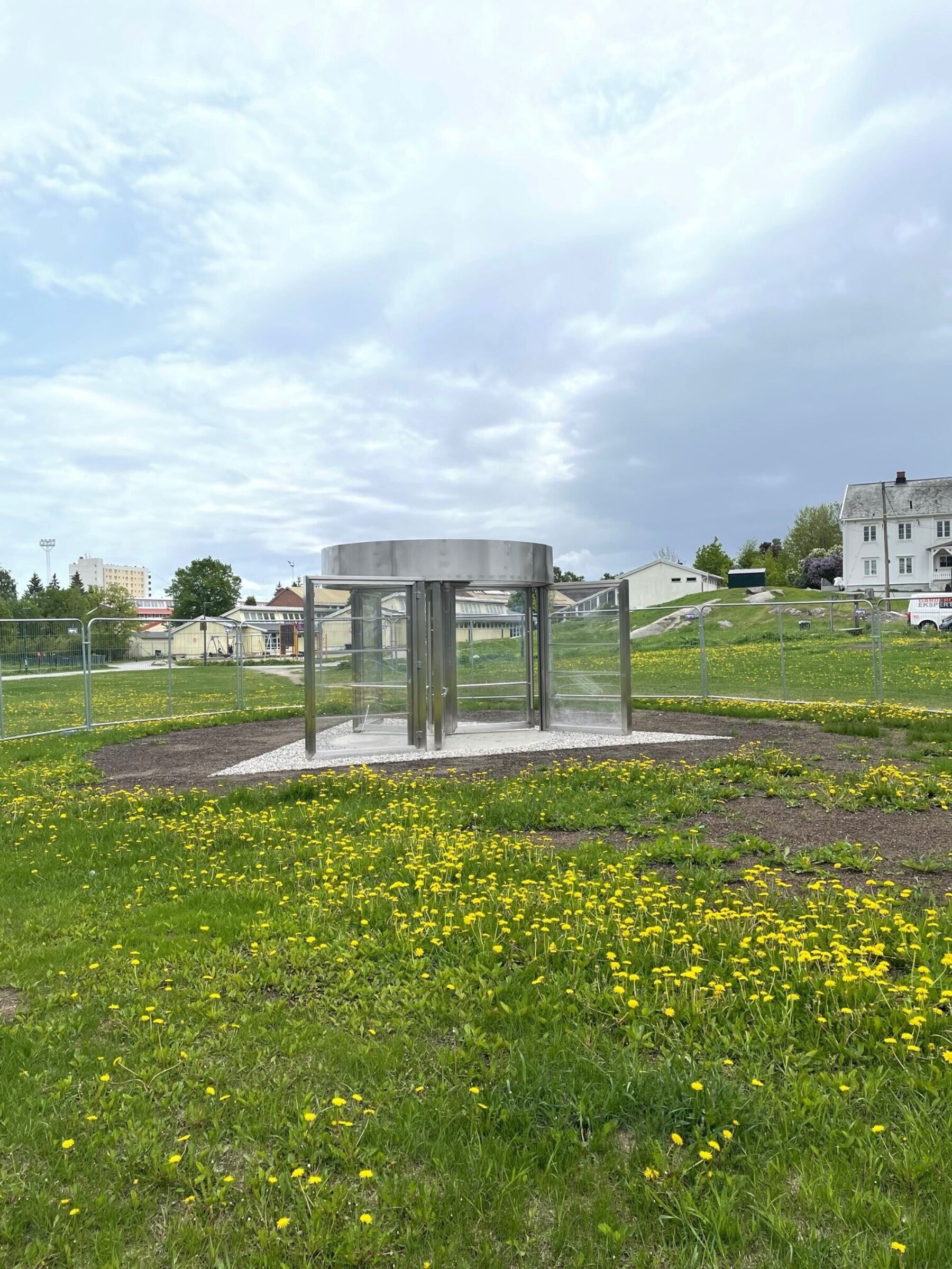 En svingdør stående ute på en gressplen med gule blomster rundt. Foto.