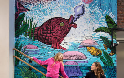 Foto av to elever som står foran et veggmaleri i et trappeløp på Slemdal skole.