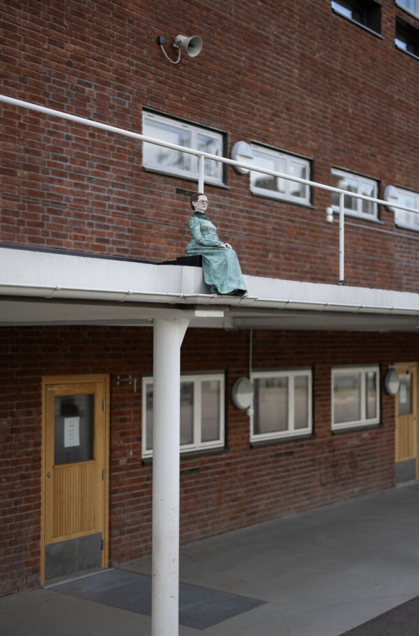 Foto av en liten skulptur av en person som sitter på et tak på Slemdal skole.