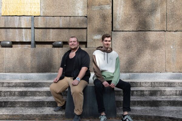 To personer sitter på en trapp. De ser mot kamera. Foto.