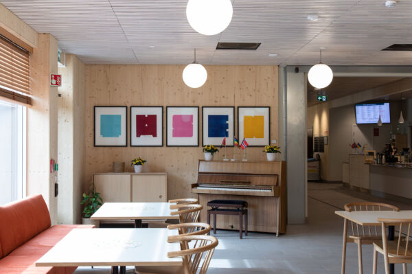 Utsnitt av en kafeteria, bildet viser flere sittegrupper, et piano og kunstverk på veggen. Foto