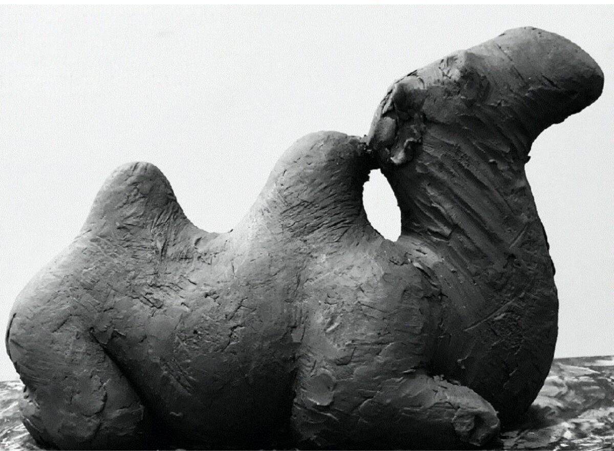 Svart-hvitt bilde av en skulptur av en kamel som ligger. Foto.