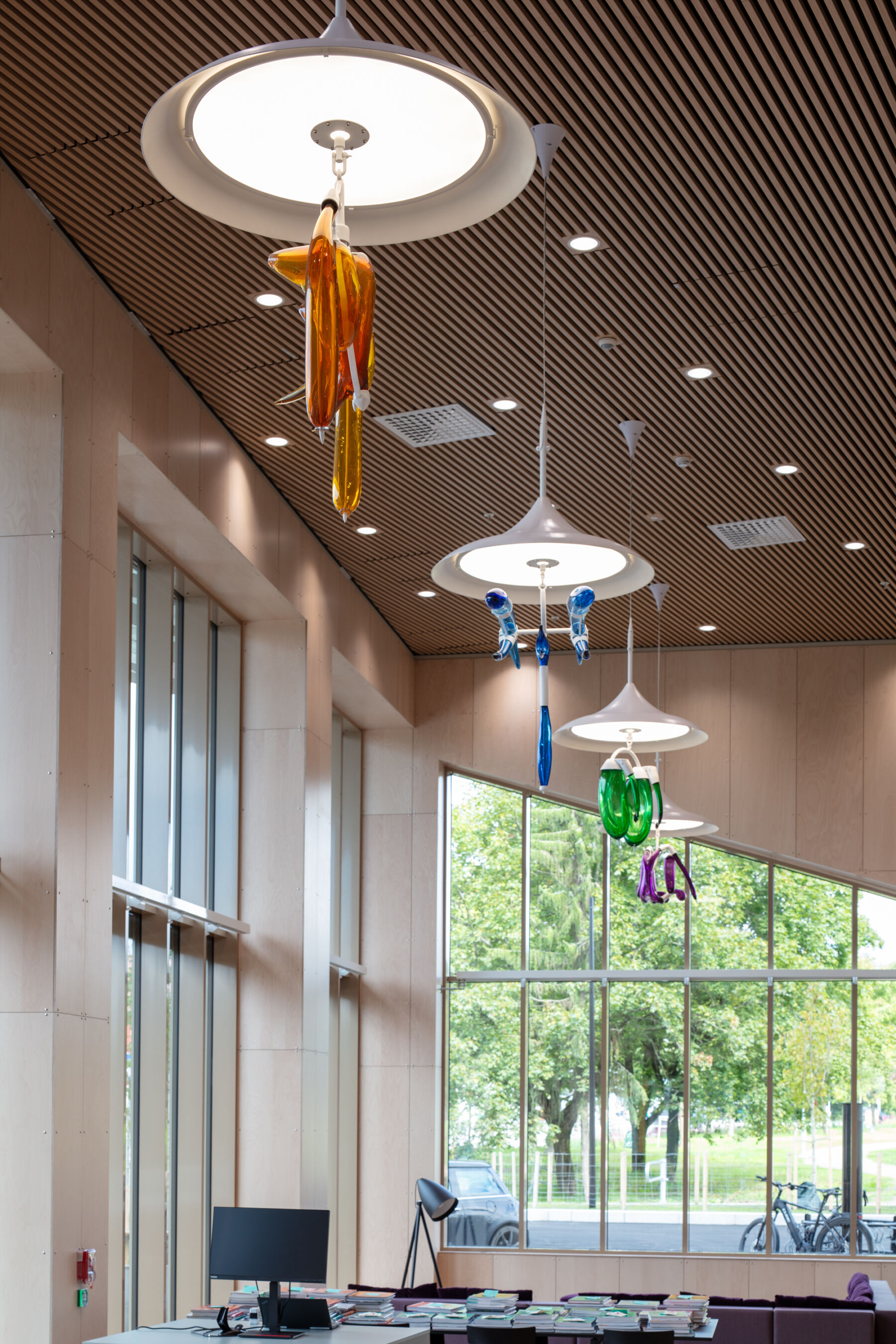 Fire skulpturelle lamper henger i taket i et bibliotek. Foto.